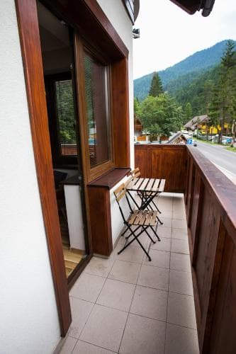 A cozy balcony with wooden furniture overlooks a serene mountain village, ideal for travelers seeking relaxation and scenic views.
