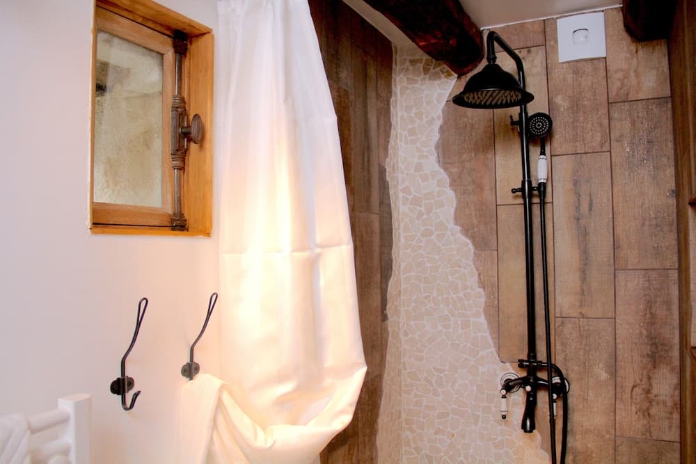 A cozy rustic bathroom features a wooden-framed mirror, a shower with mosaic tiles, and soft lighting, ideal for travelers seeking a serene and charming accommodation experience.