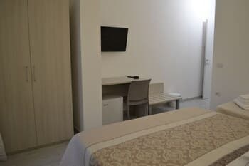 A cozy hotel room features a neatly made bed, a small desk with chairs, a mounted TV, and a wardrobe, creating a simple yet inviting atmosphere ideal for travelers seeking comfort and functionality.