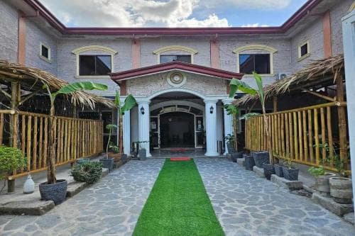 A charming tropical hotel entrance features a stone pathway lined with lush greenery and bamboo structures, creating a welcoming and serene atmosphere ideal for travelers seeking relaxation.