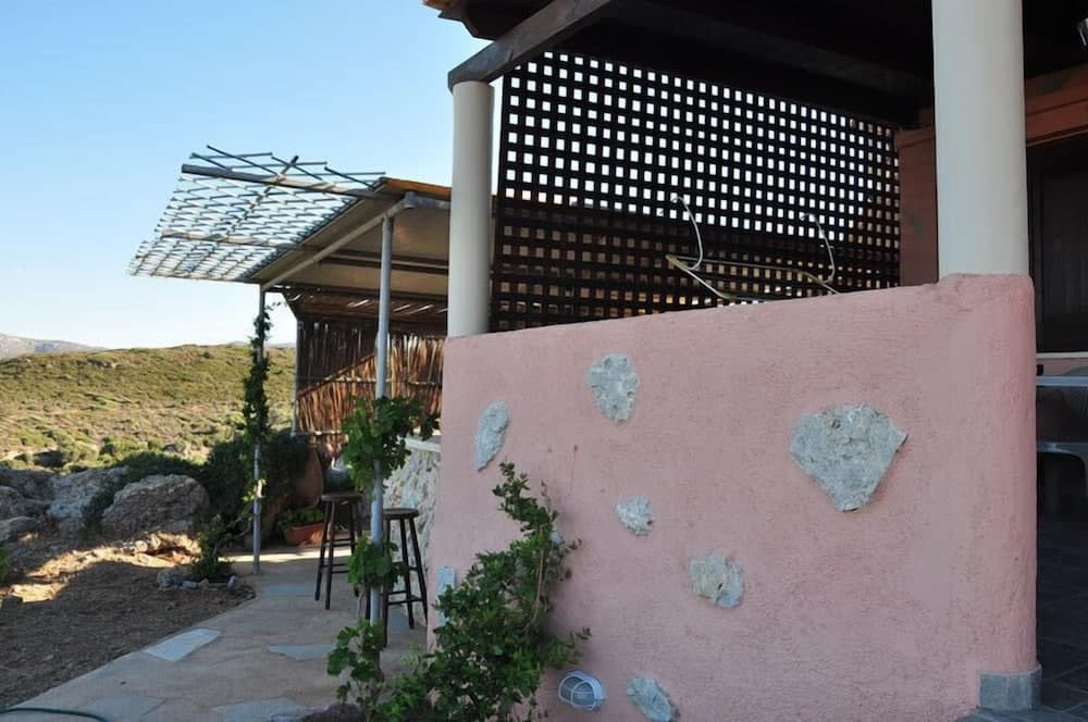 A serene outdoor patio with a pink wall adorned with stones overlooks a lush hillside, featuring wooden pergolas and greenery, ideal for a tranquil vacation retreat.