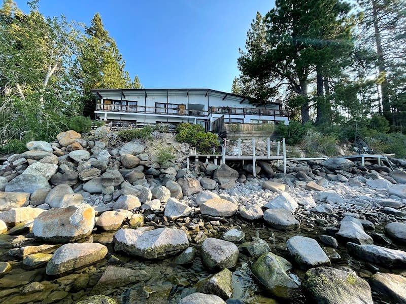 A serene lakeside holiday house surrounded by lush greenery and rocky shores, featuring a charming dock and ideal for tranquil retreats in Tahoe Vista, California.