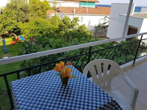 A cozy balcony with a blue checkered tablecloth and vibrant flowers overlooks a lush garden and nearby buildings, creating a serene and inviting atmosphere perfect for a relaxing vacation getaway.