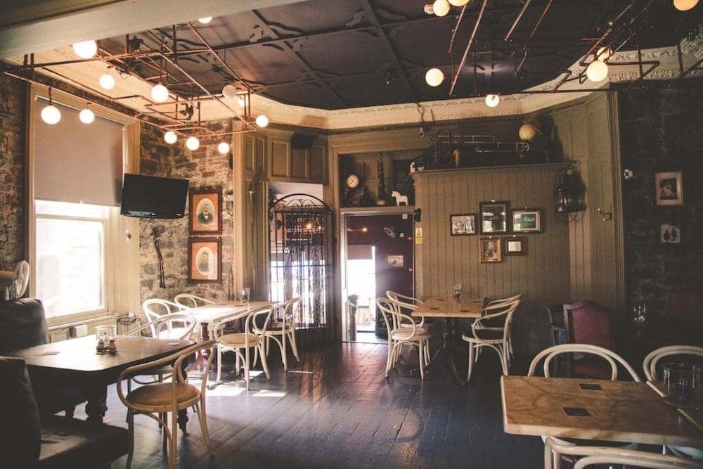 A cozy, rustic café with wooden floors, exposed brick walls, vintage decor, and warm pendant lights invites travelers to enjoy a relaxing meal or coffee in an intimate setting.