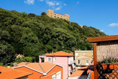 A picturesque village scene with vibrant terracotta-roofed houses nestled among lush greenery under a clear blue sky, featuring a historic castle atop the hill, ideal for travelers seeking serene cultural exploration.