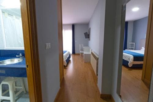 A cozy hotel room hallway with wooden floors, blue accents, and open doors revealing beds and a bathroom, ideal for travelers seeking comfortable accommodations.