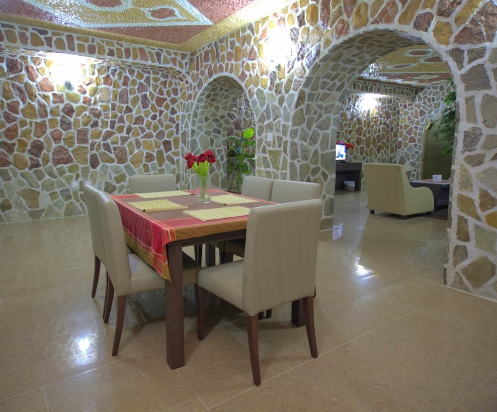 A cozy dining area with stone arches and walls, featuring a wooden table set with vibrant linens and red flowers, evokes a warm, rustic charm ideal for intimate gatherings in a unique vacation rental.