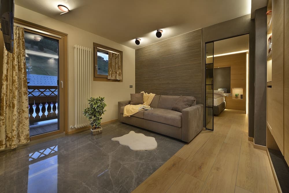 A cozy modern living space with warm lighting, a plush sofa, wooden flooring, and a balcony view, ideal for travelers seeking a comfortable and stylish accommodation.