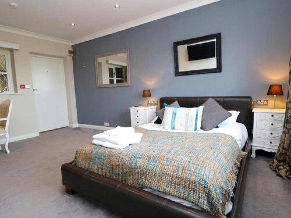 A cozy hotel bedroom features a neatly made bed with patterned bedding, white bedside tables with lamps, and a calming blue wall, ideal for travelers seeking comfort and relaxation.