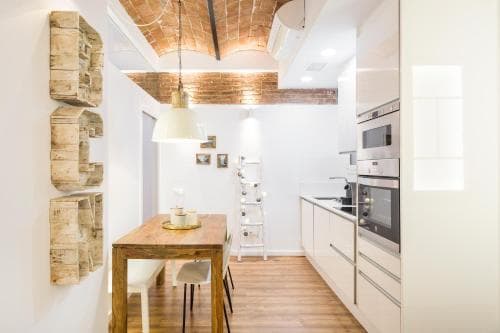 A cozy modern kitchen with exposed brick ceiling, wooden flooring, and stylish decor creates an inviting atmosphere, perfect for travelers seeking a charming urban retreat.