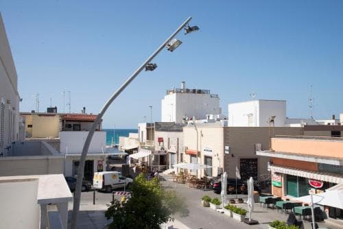 A vibrant coastal town square bathed in sunlight features outdoor cafes, modern streetlights, and a serene sea view, ideal for travelers seeking a relaxing seaside retreat.