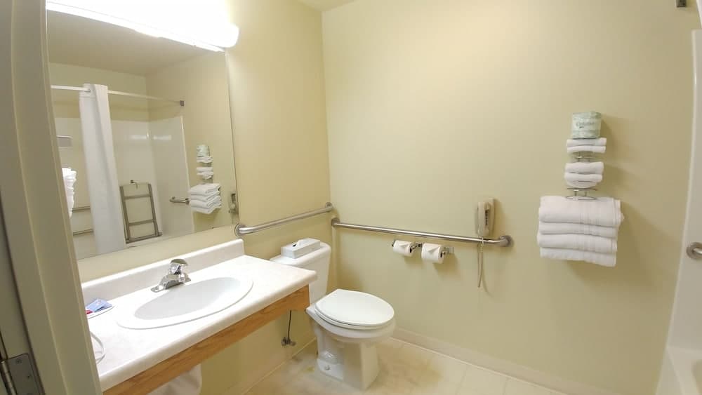 A clean, accessible hotel bathroom features a sink, toilet with grab bars, neatly folded towels, and a mirror, ideal for travelers seeking comfort and convenience.
