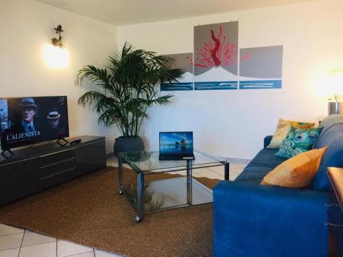 A cozy living room with a blue sofa, vibrant pillows, a glass coffee table, and modern artwork creates a welcoming atmosphere, ideal for travelers seeking comfort in a stylish apartment setting.
