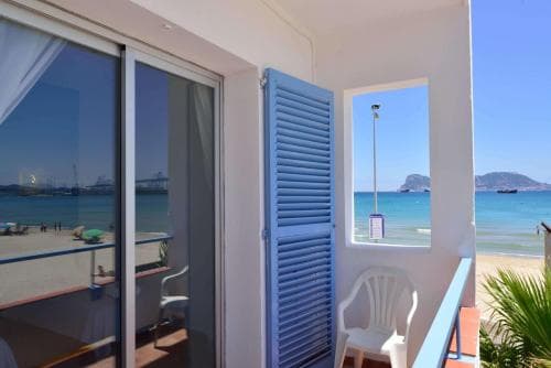 A cozy balcony with blue shutters overlooks a serene beachfront scene, perfect for travelers seeking relaxation near the sea.