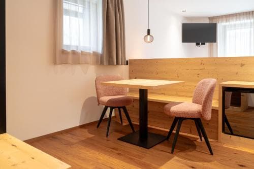 A cozy modern dining area with wooden floors, pink chairs, and a sleek table invites travelers to relax in a minimalist hotel room setting.