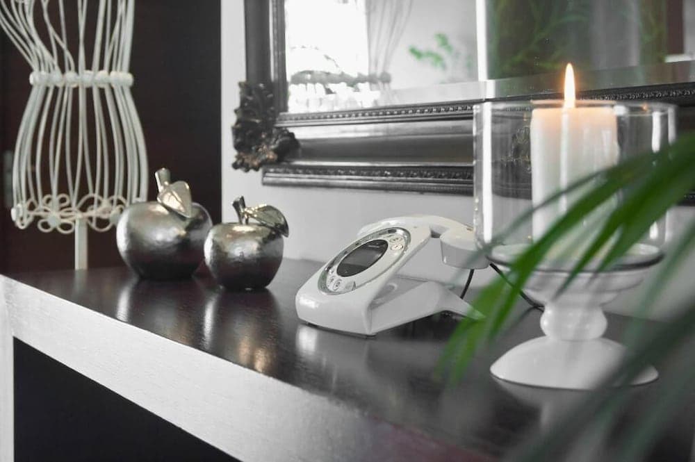 A cozy hotel room corner features a sleek desk adorned with decorative apples, a modern phone, a lit candle, and greenery, creating an inviting atmosphere ideal for travelers seeking comfort and style.