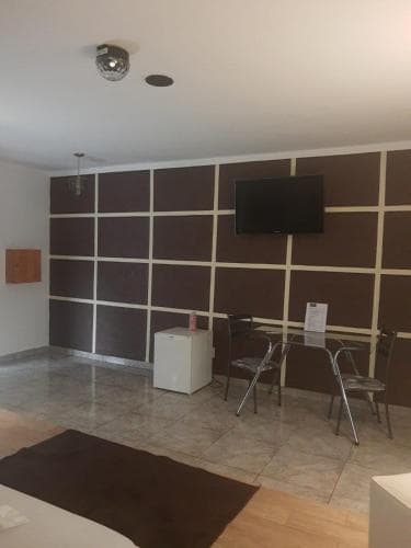 A cozy hotel room features a tiled floor, a wall-mounted TV, and modern furnishings, creating a welcoming atmosphere ideal for travelers seeking comfort and convenience.