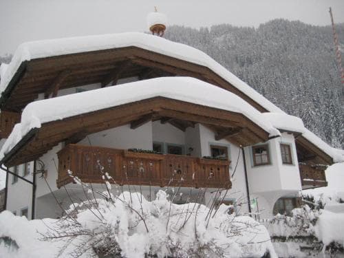 A cozy snow-covered chalet with wooden balconies nestled in a serene alpine setting offers a picturesque winter retreat for travelers seeking a tranquil mountain escape.