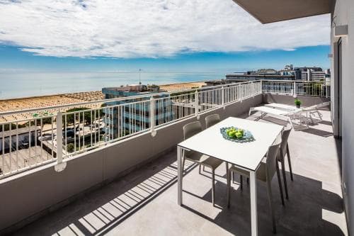 A serene rooftop terrace with a white dining table set against a backdrop of the sea and urban skyline, perfect for a relaxing coastal getaway.