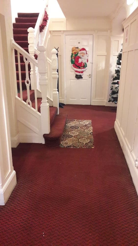 A cozy, festive hallway adorned with Christmas decorations, featuring a Santa-themed door hanging, a patterned rug, and a staircase, ideal for travelers seeking a warm, holiday atmosphere in a guesthouse or hotel.