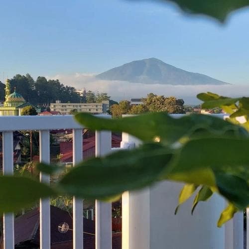 A serene balcony view captures a misty mountain backdrop over a quaint town, framed by lush greenery, ideal for travelers seeking peaceful retreats.
