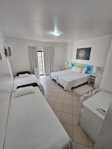 A cozy hotel room with tiled floors, white bedding, a colorful wall mural, and a balcony view, ideal for travelers seeking comfort and relaxation.