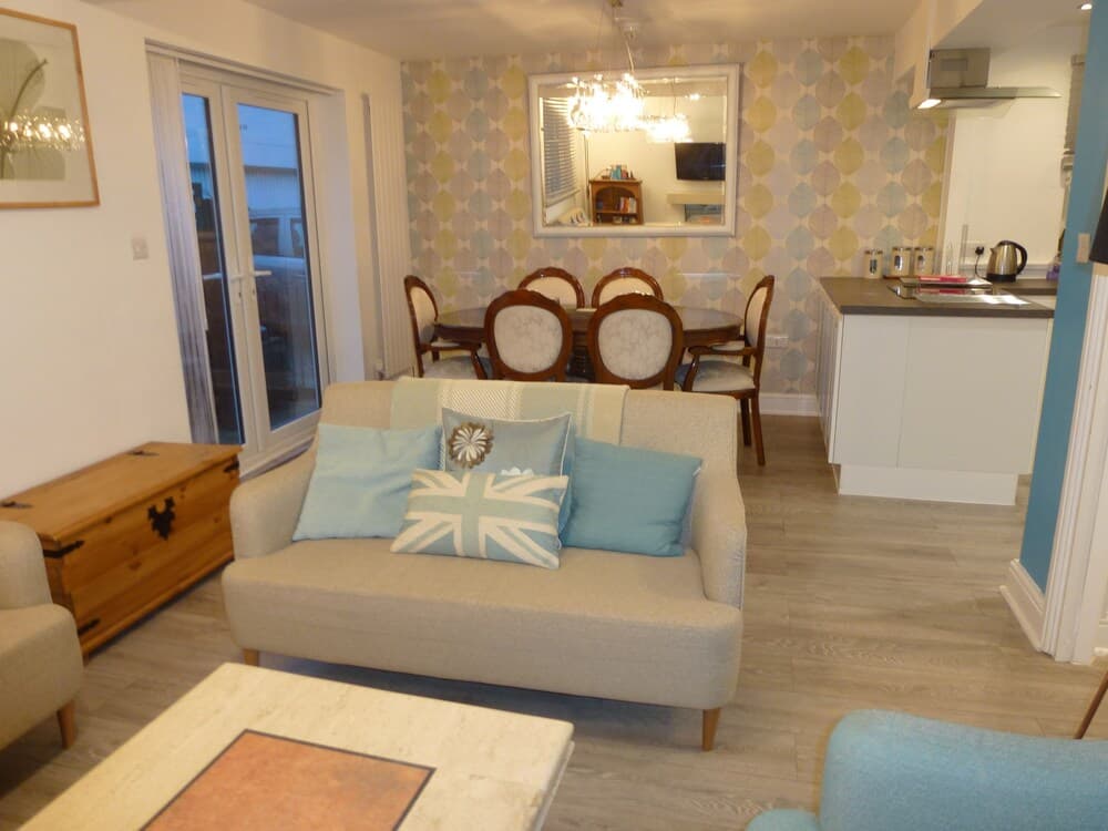 A cozy living space with a Union Jack pillow, light blue decor, and a dining area in the background offers a welcoming atmosphere for travelers seeking a homey vacation rental.