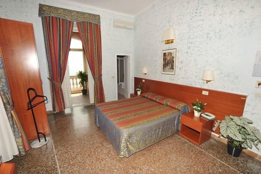 A cozy hotel room with patterned curtains, wooden furnishings, and potted plants exudes a warm and inviting atmosphere, ideal for travelers seeking comfort during their stay.