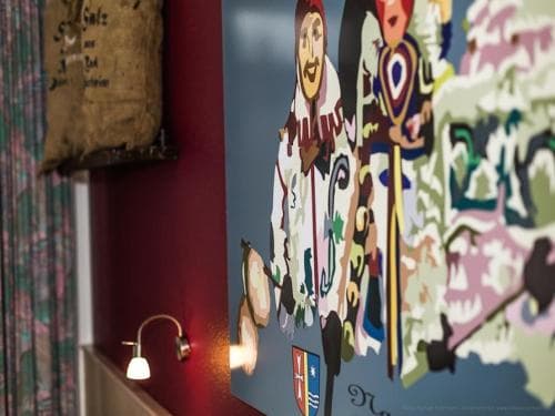 A cozy indoor setting features vibrant folk art paintings of traditional figures alongside rustic decor elements like a sack and warm lighting, ideal for cultural tourism enthusiasts exploring local heritage sites.