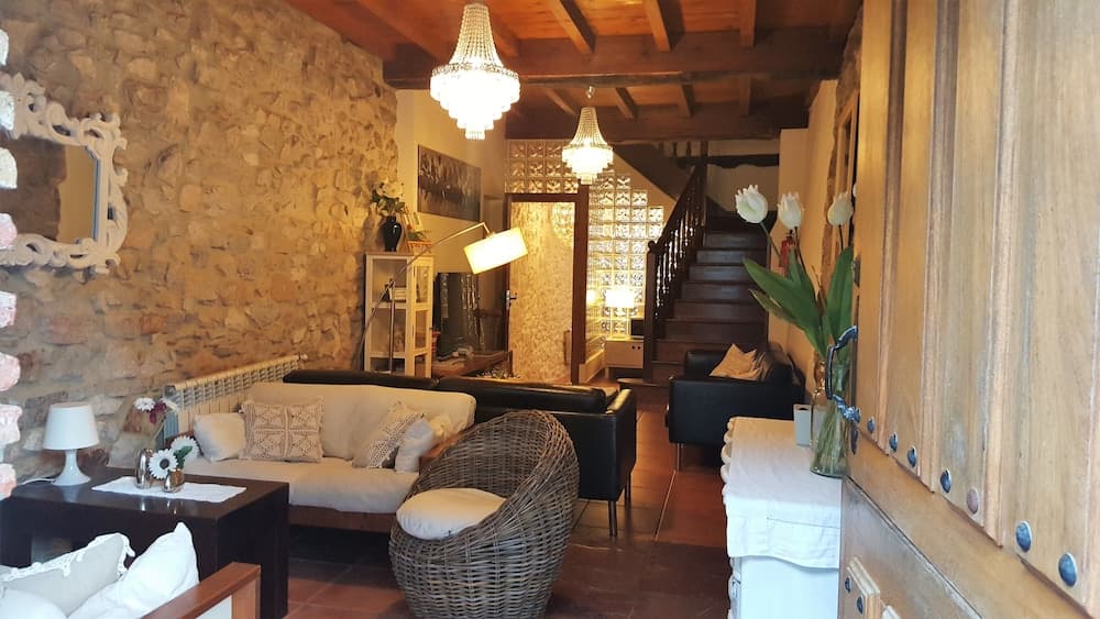 A cozy rustic living room with stone walls, wooden beams, elegant chandeliers, and comfortable seating creates a warm and inviting atmosphere ideal for a relaxing getaway or vacation rental.