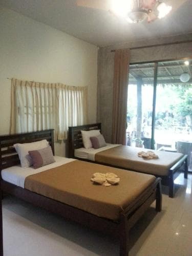 A cozy hotel room with two neatly arranged beds, soft lighting, and a view of lush greenery through glass doors, ideal for travelers seeking relaxation in a serene environment.
