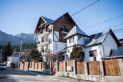 A quaint alpine village street features charming wooden and white houses with sloped roofs, set against a backdrop of towering mountains, ideal for travelers seeking a serene mountain retreat.