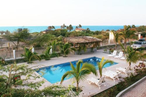 A serene tropical resort features a vibrant blue pool surrounded by palm trees and lounge chairs, overlooking the ocean, ideal for a relaxing beach vacation getaway.