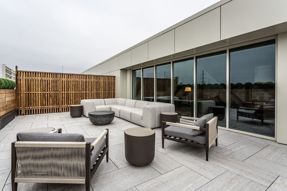 A serene rooftop patio features modern outdoor furniture and a wooden privacy fence, creating an inviting space for relaxation or social gatherings near large glass windows.