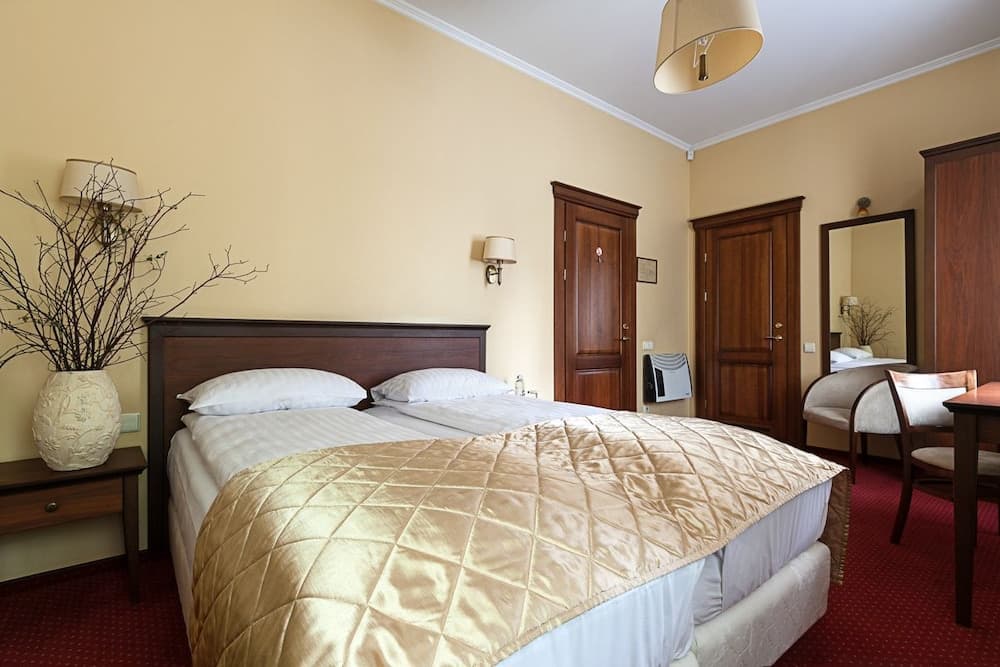 A cozy hotel room features a neatly made bed with a gold quilt, wooden furnishings, and warm yellow walls, creating an inviting atmosphere ideal for travelers seeking comfort and relaxation.