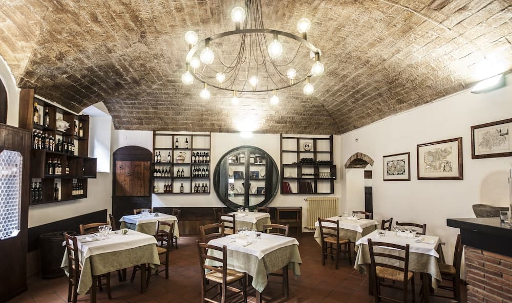 A cozy, rustic restaurant with arched brick ceilings, warm lighting, neatly arranged tables, and shelves stocked with wine bottles creates an inviting atmosphere perfect for travelers seeking an authentic dining experience.