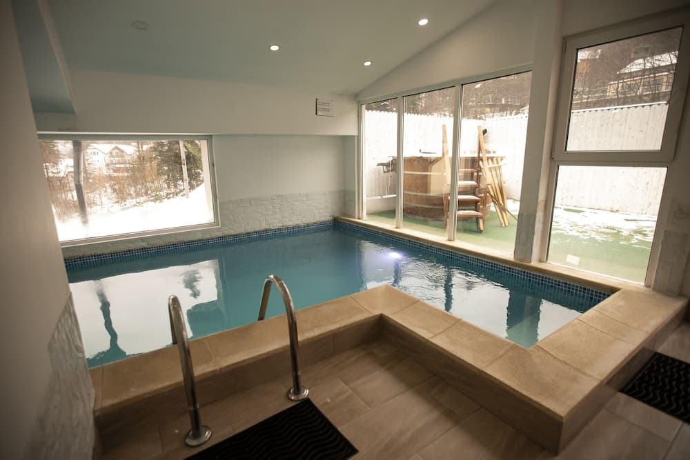 A serene indoor pool with a tiled deck and large windows offering a snowy outdoor view, ideal for relaxation and winter getaways.