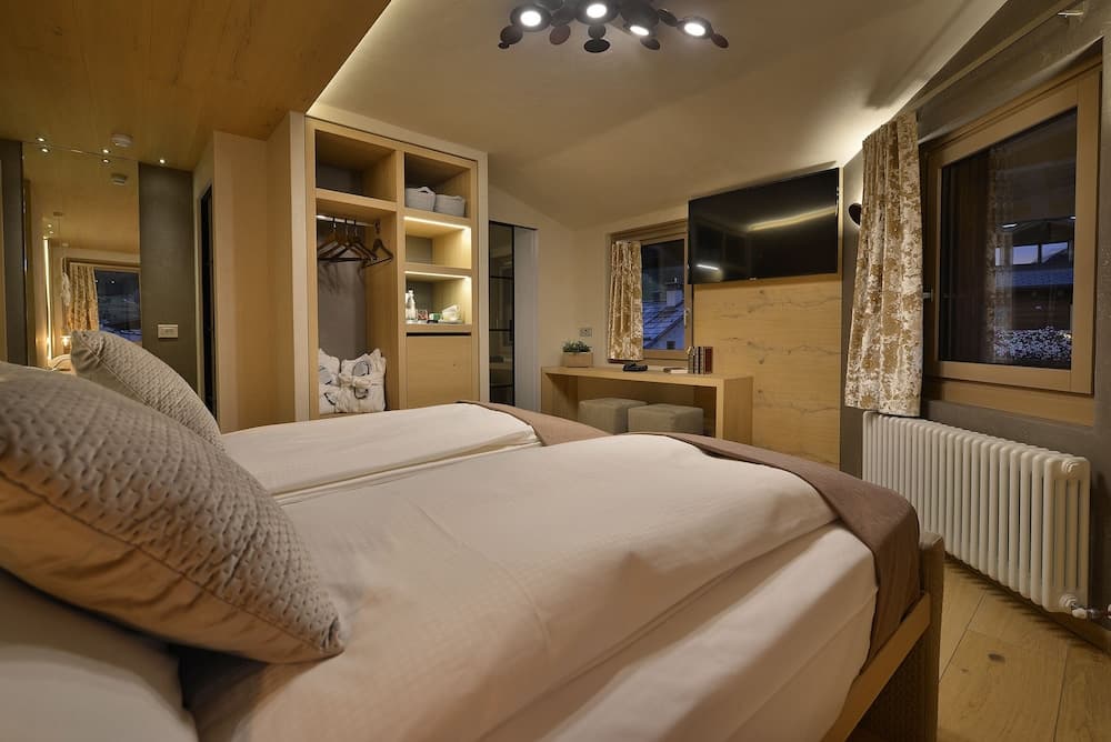 A cozy hotel room with wooden accents, neatly made twin beds, a built-in closet, and a desk by the window, ideal for travelers seeking comfort and functionality.