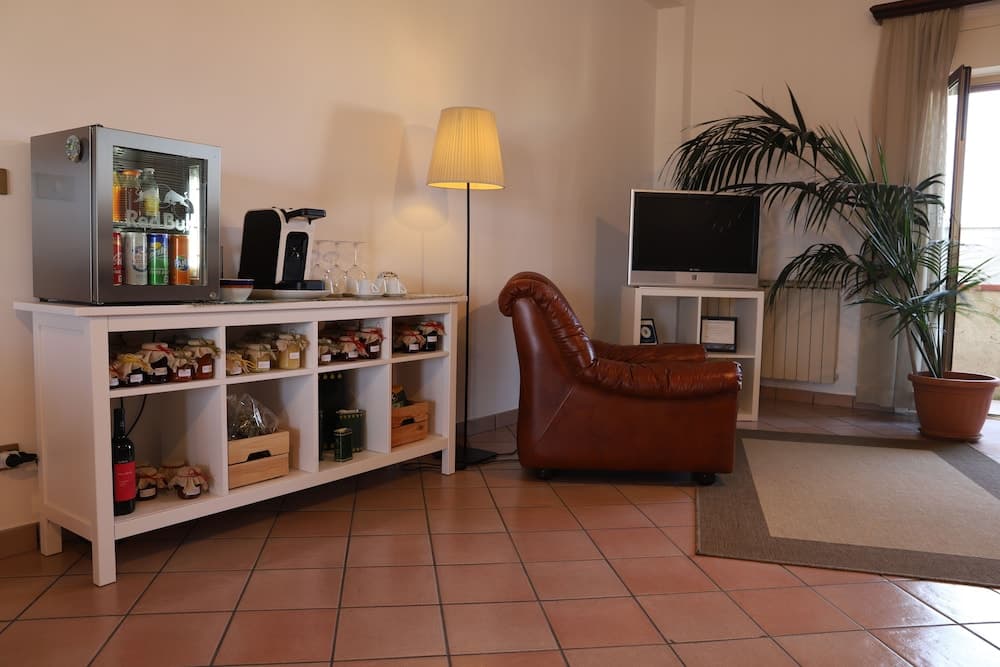 A cozy lounge area features a leather armchair, a stocked refreshment station with a mini-fridge, and a flat-screen TV, creating a welcoming atmosphere ideal for travelers seeking relaxation in a hotel or guesthouse setting.