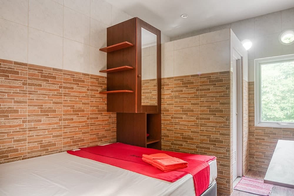 A cozy bedroom with brick-patterned walls, a wooden shelving unit, and a neatly made bed with red accents invites travelers seeking a comfortable and stylish accommodation.
