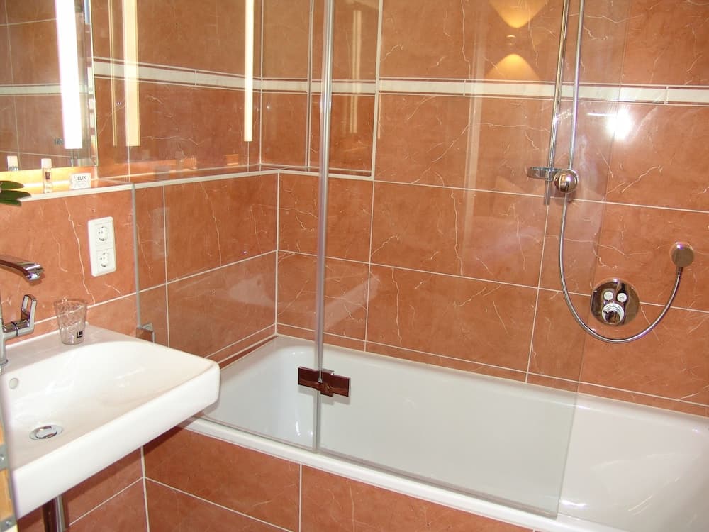 A cozy hotel bathroom features warm-toned marble tiles, a sleek bathtub with a glass shower screen, and a modern sink, ideal for travelers seeking comfort and cleanliness.