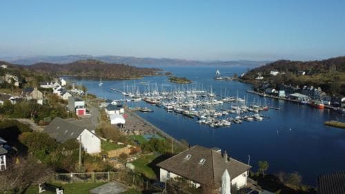 A serene coastal village with quaint houses and a bustling marina framed by lush hills under a clear blue sky, ideal for travelers seeking a peaceful seaside retreat.