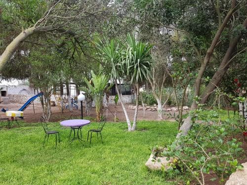 A serene garden oasis features lush greenery, a purple table with chairs, and a playful slide, ideal for a relaxing family getaway or a tranquil retreat.