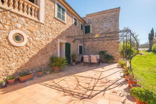 A charming stone villa with a sunlit patio, lush greenery, and cozy seating offers a serene retreat ideal for a relaxing countryside getaway.