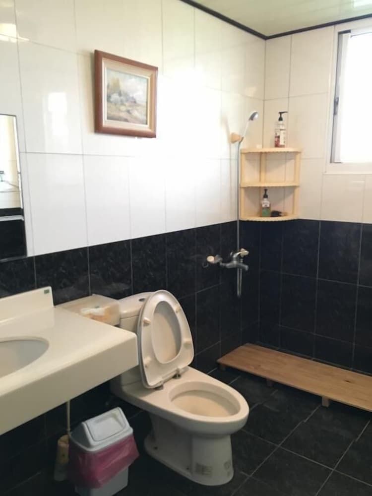 A compact bathroom with black and white tiled walls, featuring a toilet, sink, wooden bench, and shower area, exudes a practical and cozy atmosphere ideal for travelers seeking functional accommodations.