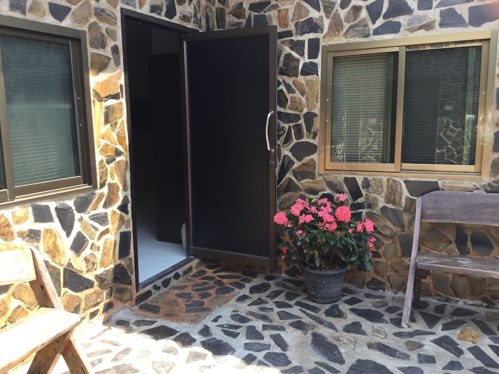 A cozy stone-walled patio with a rustic bench, vibrant pink flowers in a pot, and an inviting open door creates a serene retreat perfect for travelers seeking a peaceful getaway.