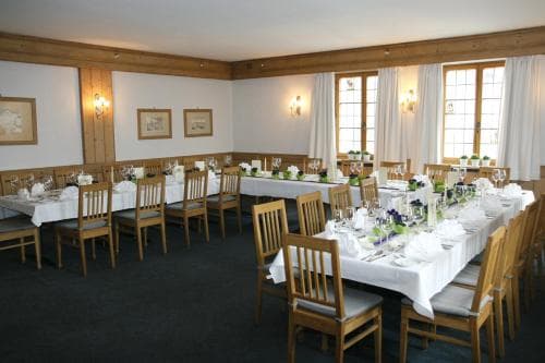 A cozy banquet hall with wooden accents, long tables set for dining, soft lighting, and large windows draped in white curtains, ideal for intimate gatherings or small conferences.