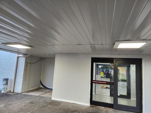 A utilitarian indoor space with a concrete floor, white walls, and a glass door leading to a brightly lit store, ideal for travelers seeking quick access to supplies or services in a functional, no-frills environment.