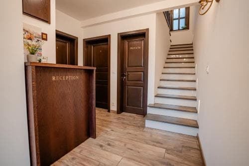 A cozy hotel reception area features wooden floors, a reception desk, and a staircase leading to upper levels, creating a welcoming atmosphere ideal for travelers seeking comfort and convenience.