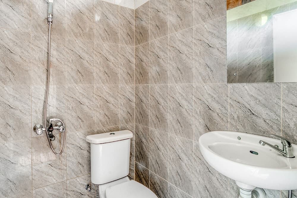 A modern bathroom with marble-patterned tiles features a sleek white toilet, sink, and showerhead, ideal for travelers seeking clean and stylish accommodations.